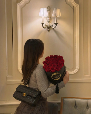 Woman holding a bouquet of red flowers and a black handbag in an elegant interior setting.